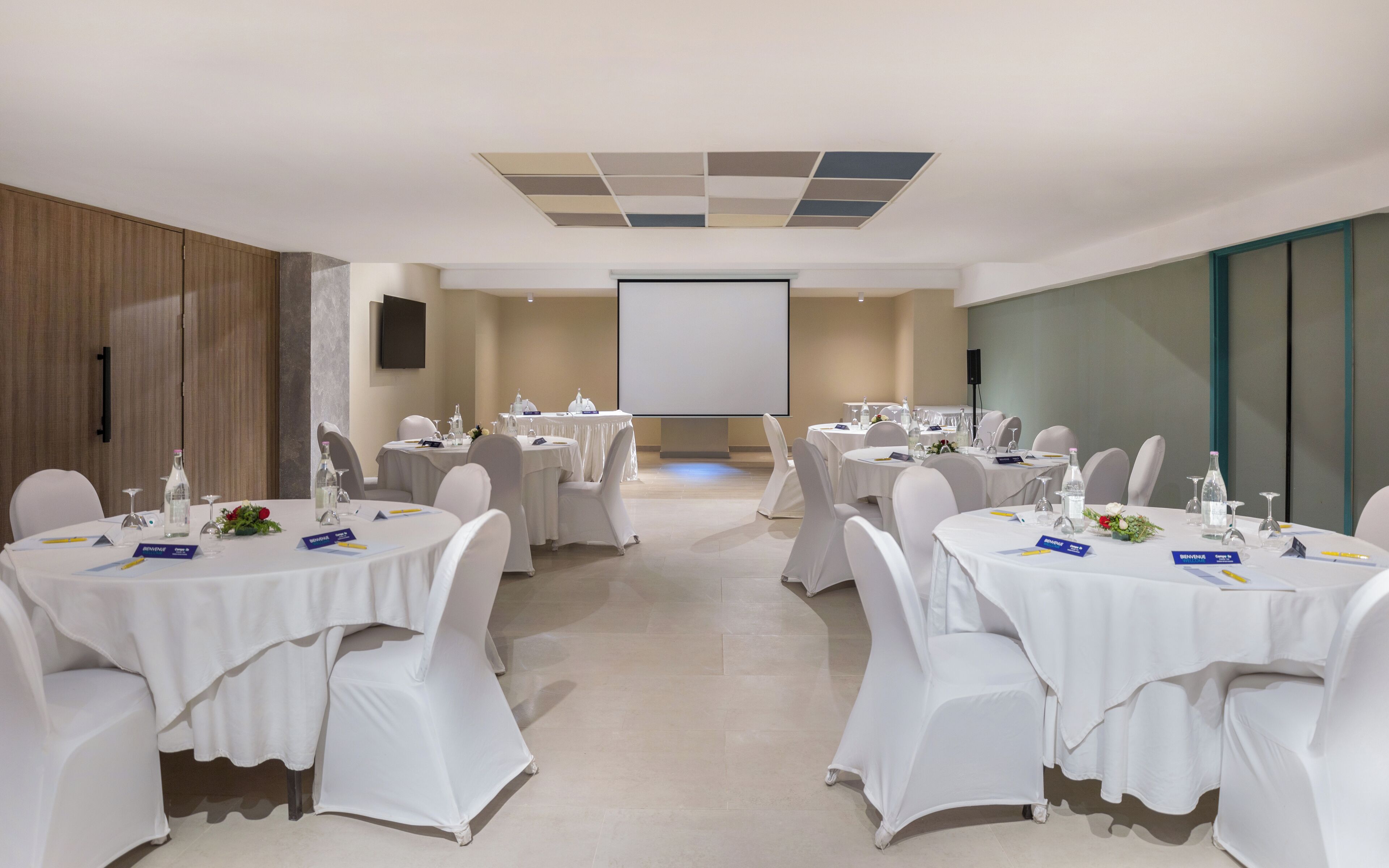 A conference room with round tables, white chairs, and a projector screen.