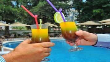 Two people holding glasses of drinks with straws and lime slices by a pool.
