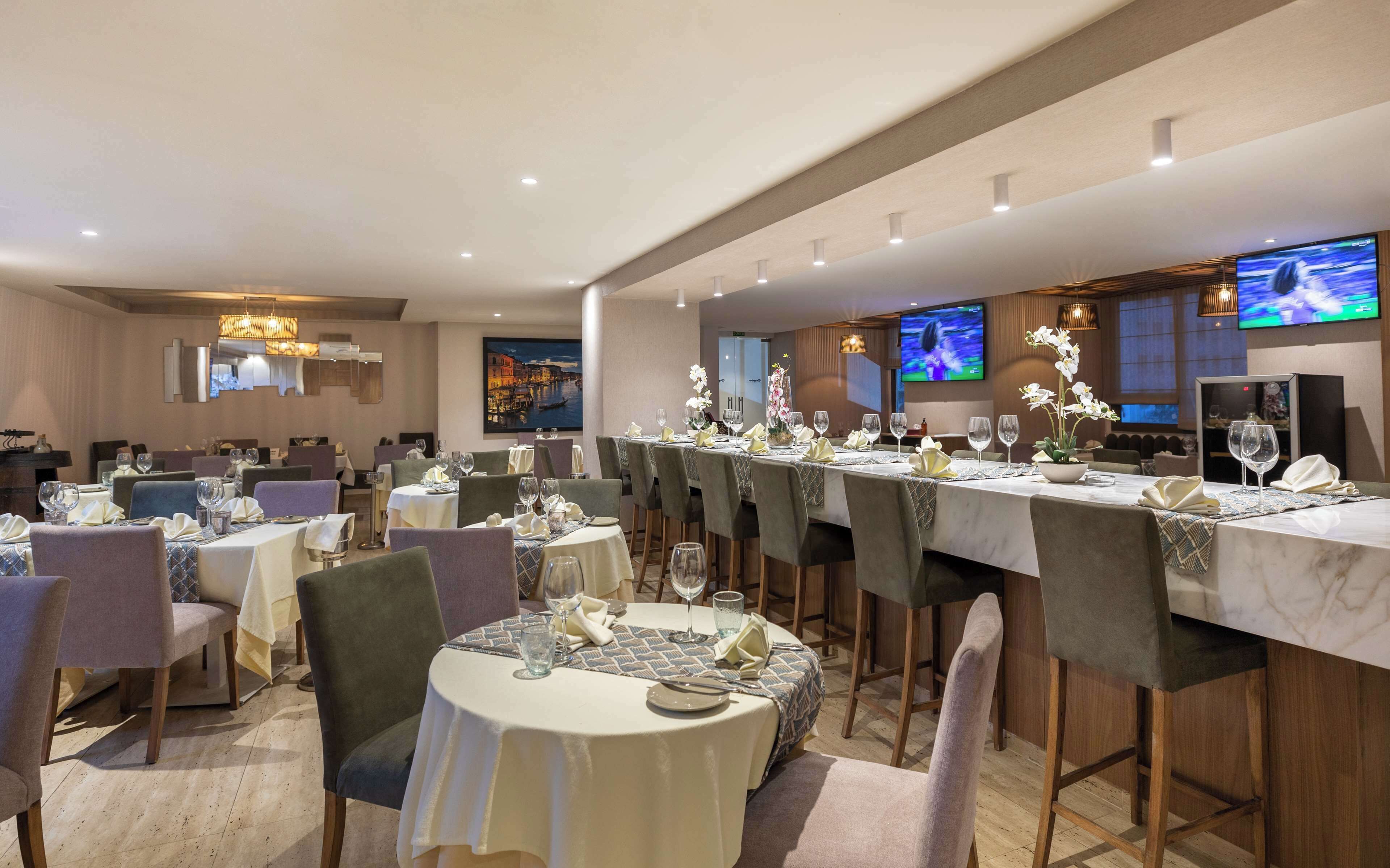Un restaurante con varias mesas dispuestas para comer, equipado con copas de vino y cubiertos.
