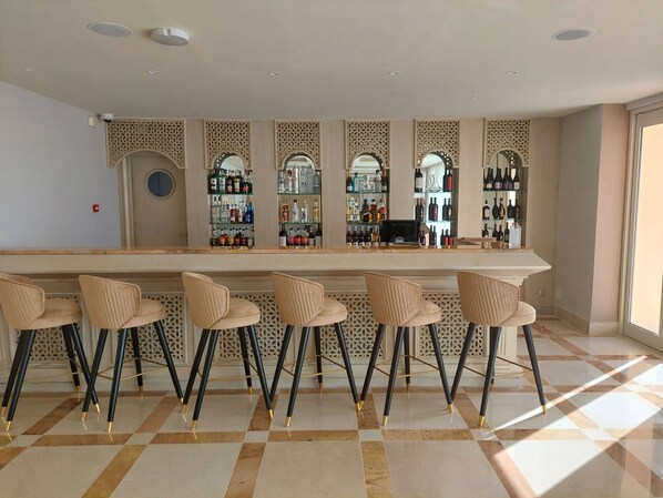 A bar area with a long counter, multiple shelves of liquor bottles, and four bar stools.