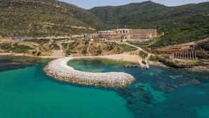 A coastal resort with a large building, a rocky beach, and a clear turquoise sea. - Royal Tulip Korbous Bay Thalasso & Springs (Qurbus)