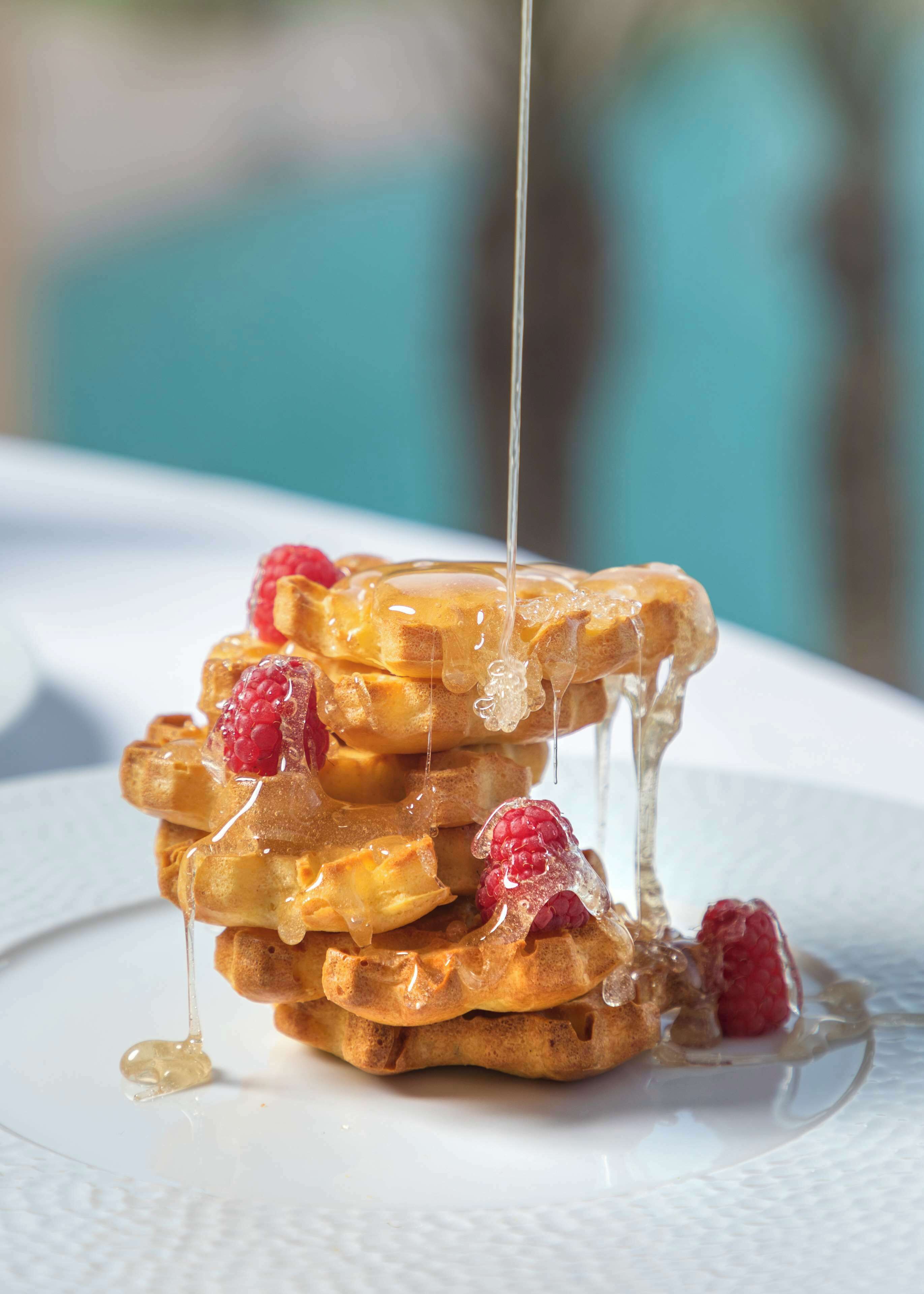 Una pila de waffles con almíbar y frambuesas.