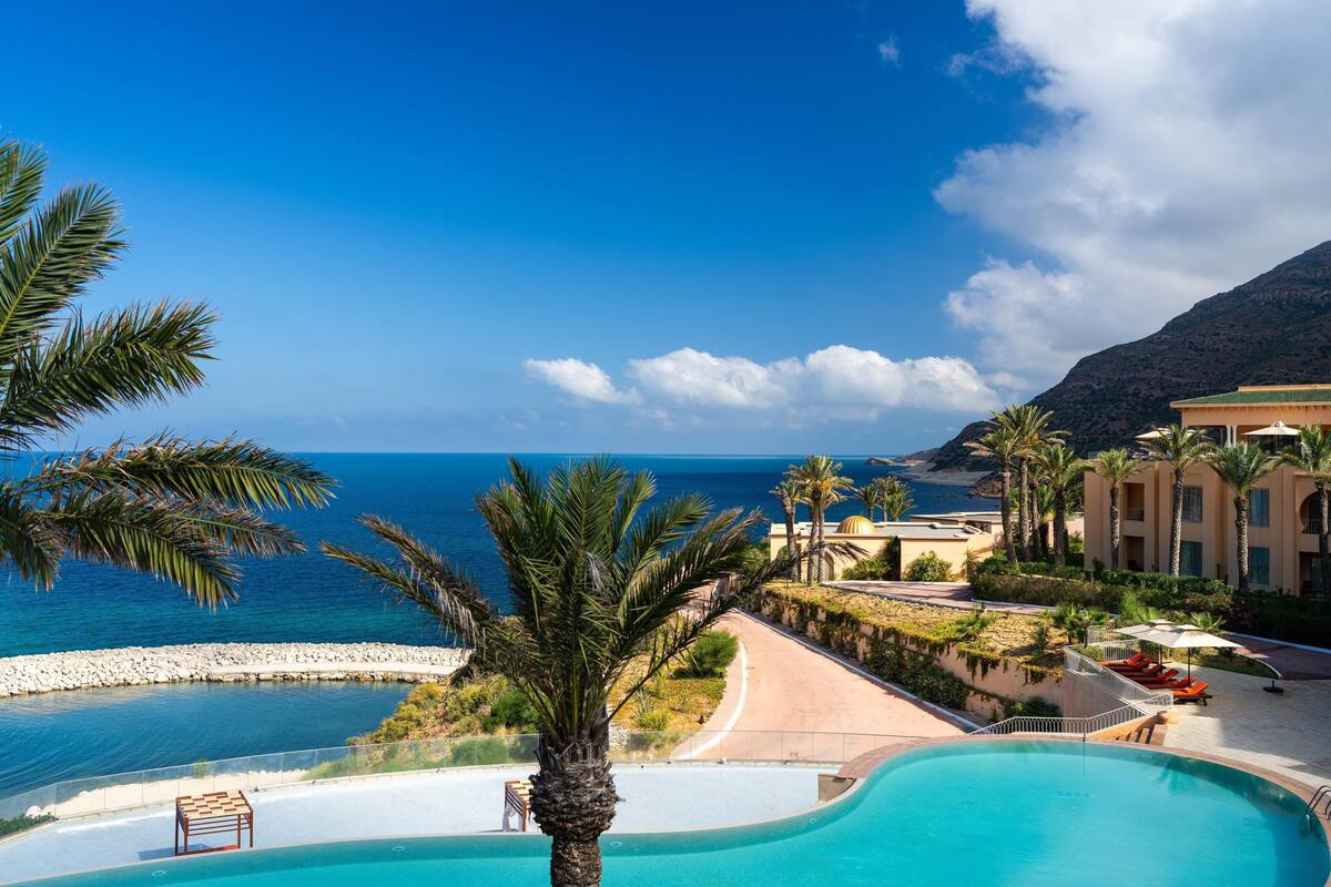 A resort with a pool, palm trees, and a view of the sea.
