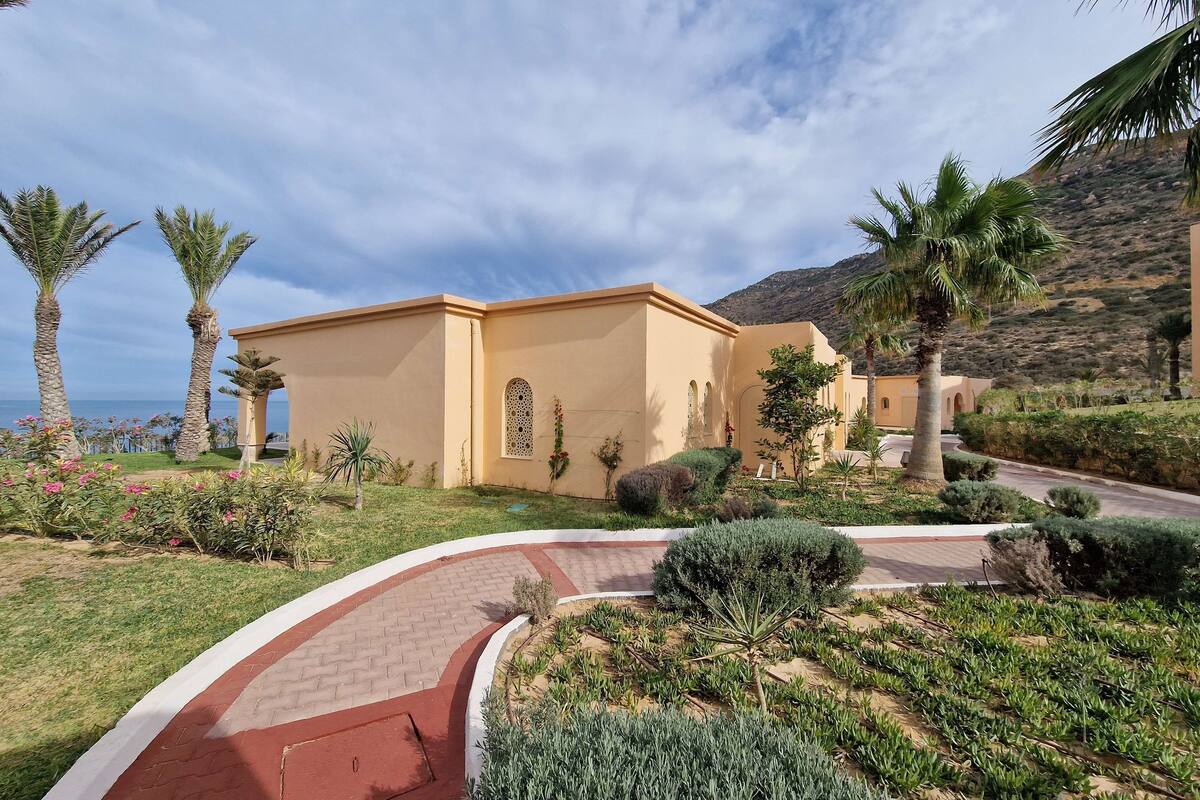 A building with a curved pathway leading to it, surrounded by palm trees and well-maintained landscaping.