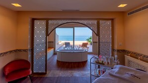 A spa room with a circular hot tub, a red chair, and a view of the beach. - Royal Tulip Korbous Bay Thalasso & Springs (Qurbus)