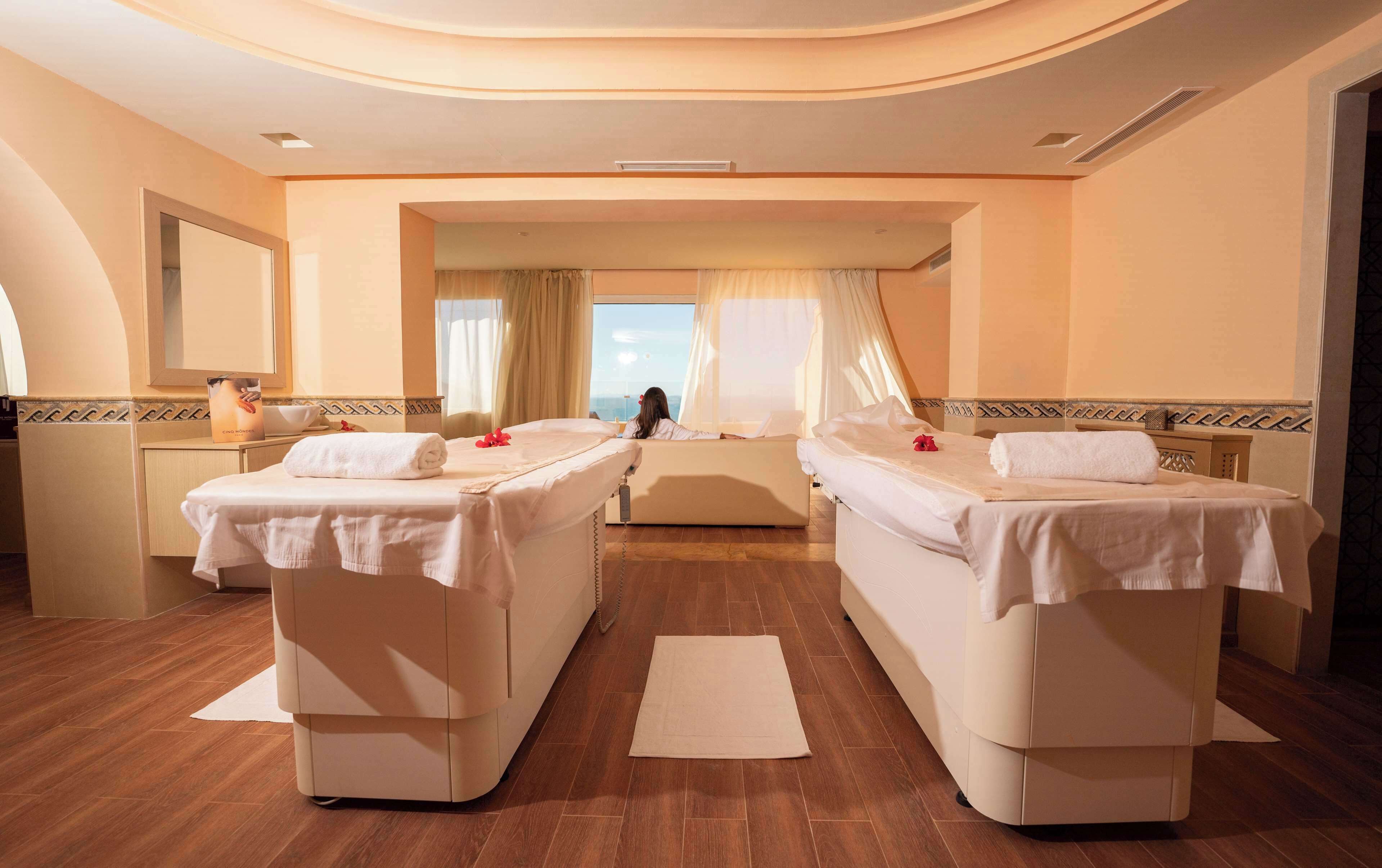 A hotel room with two beds, a large window, and a mirror.