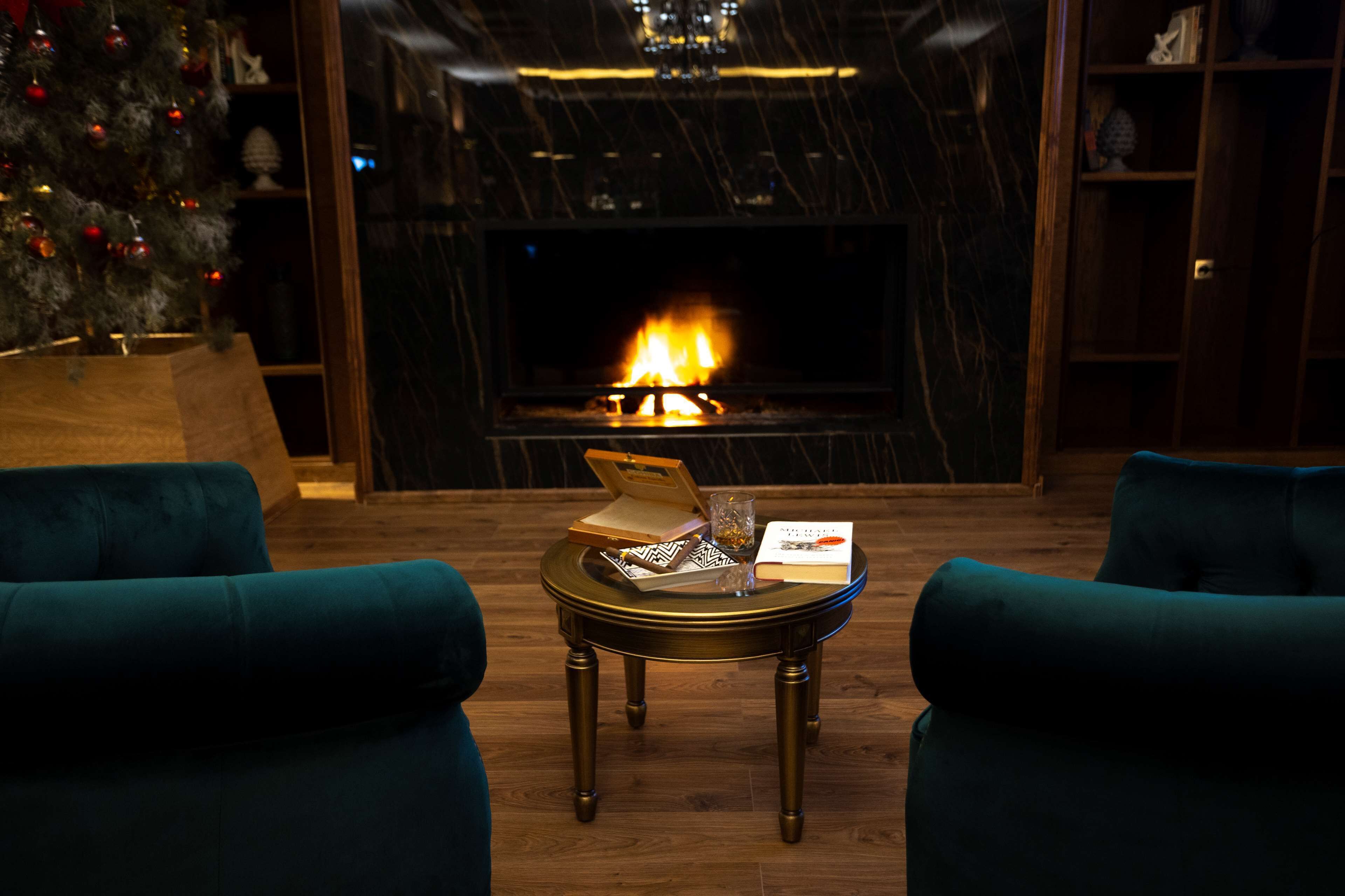 A cozy room with a fireplace, two teal armchairs, and a small round table with a book and a glass.