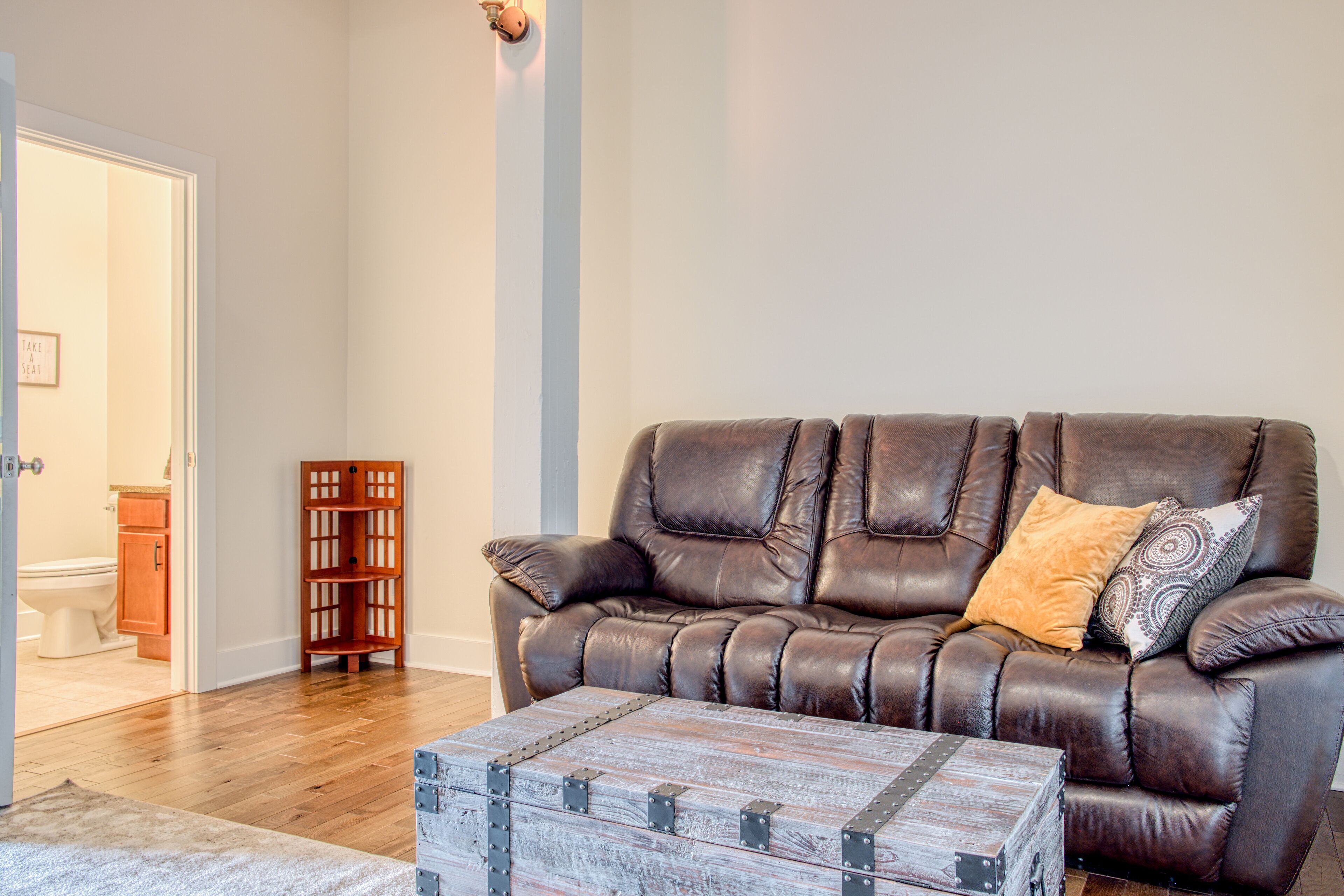 A living room with a brown leather sofa, a wooden chest, and a small wooden shelf.