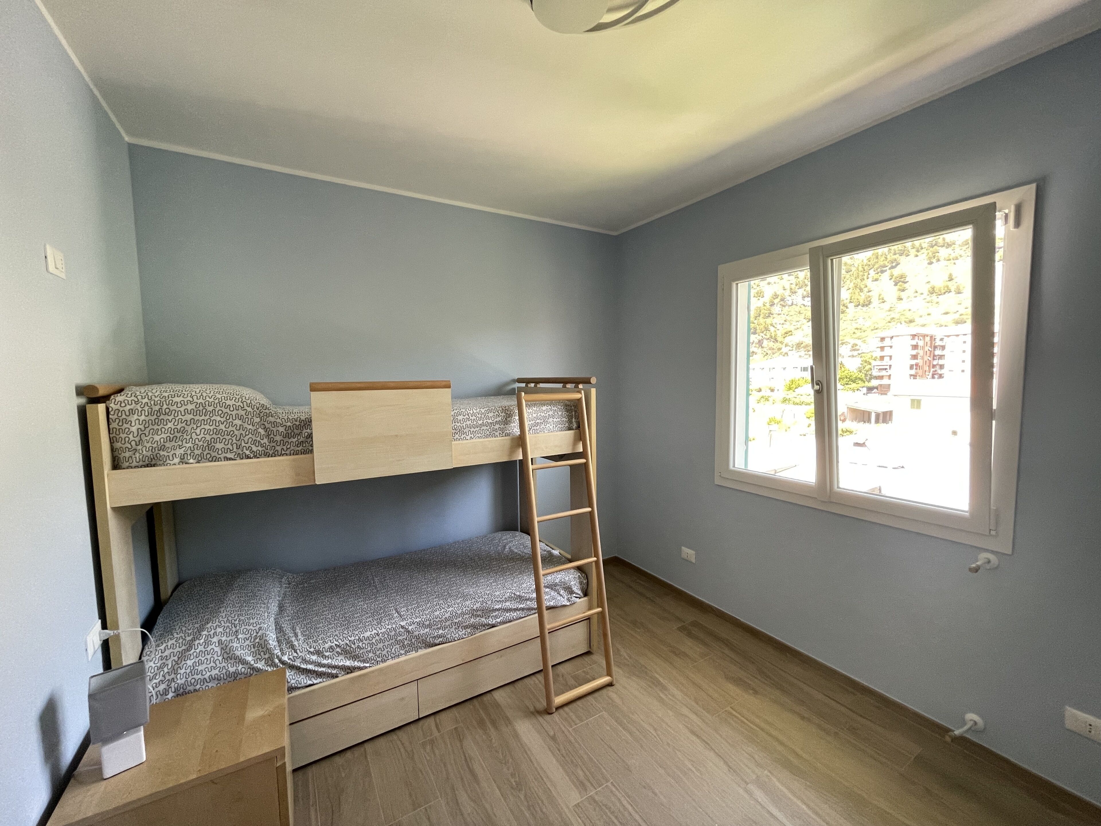 Una stanza con un letto a castello, una finestra vista edifici e un pavimento in legno.