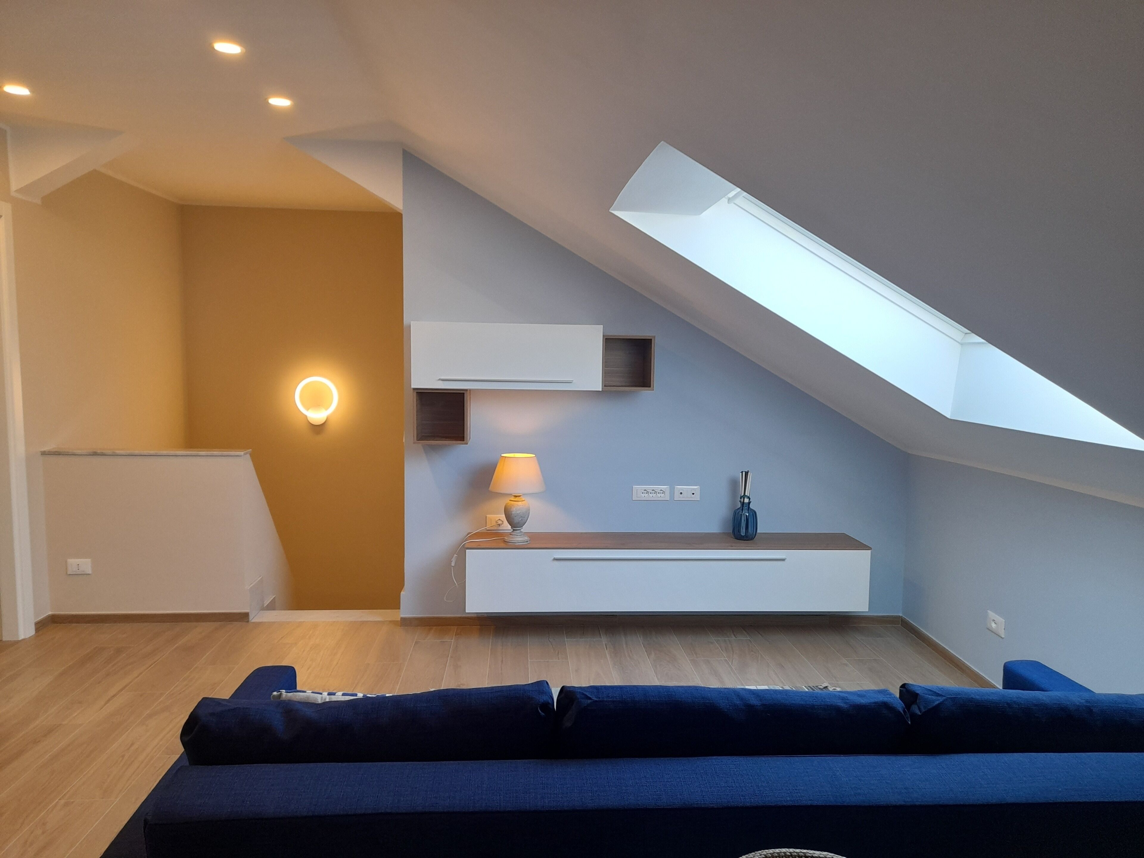 Un salon moderne doté d’un plafond en pente, d’une banquette intégrée, d’une lampe et d’une étagère fixée au mur.