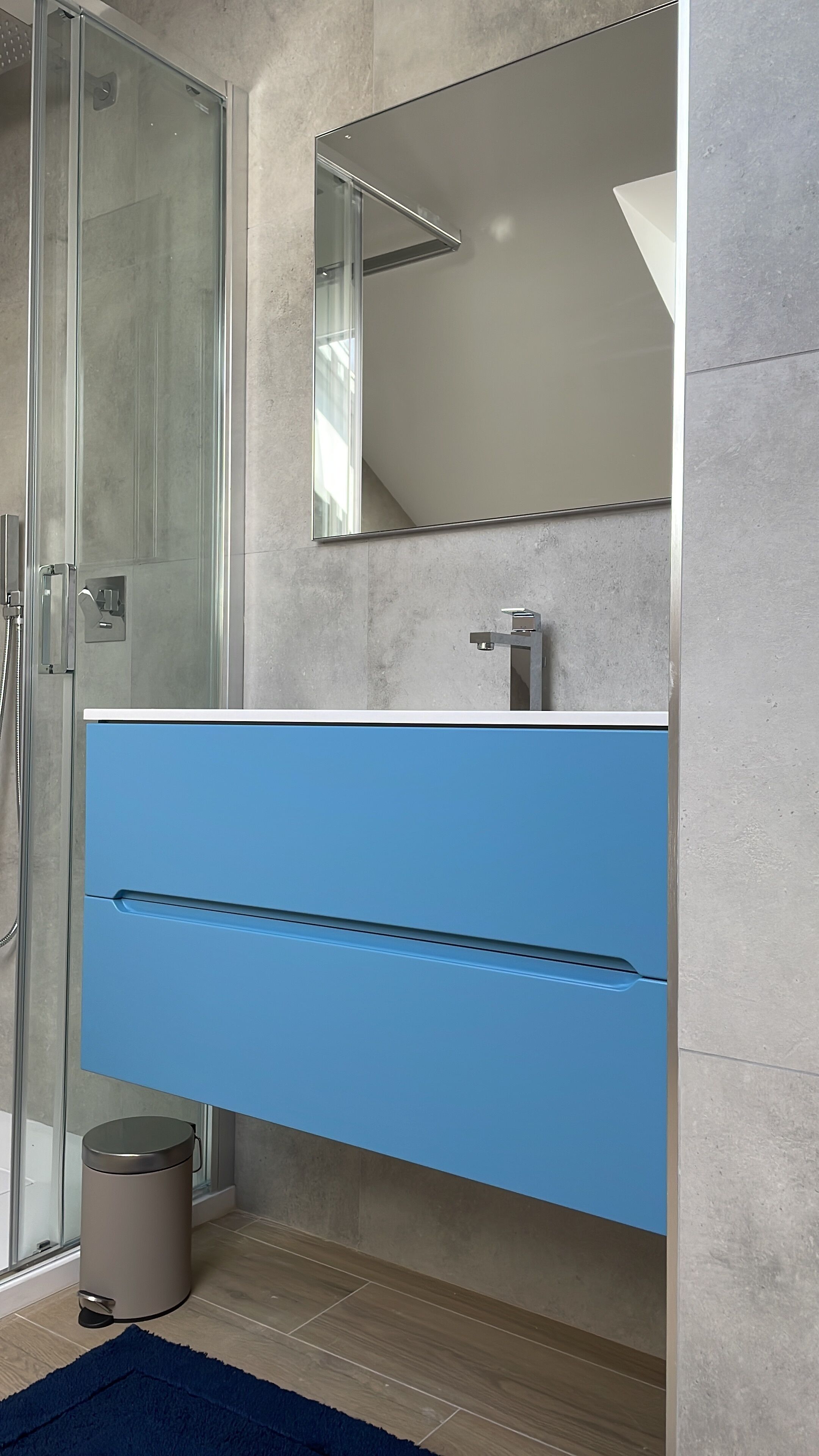 A modern bathroom with a glass shower enclosure, a blue vanity with a mirror, and a stainless steel sink.