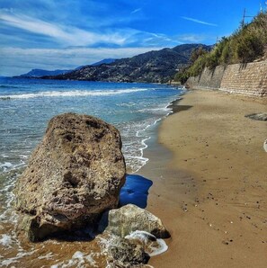 Una platja amb aigua blava cristal·lina, una gran roca al primer pla i un mur de pedra a la dreta.