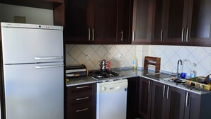 Una cocina con alacenas de madera oscura, un refrigerador blanco Bosch, una estufa y un lavabo con escurreplatos.