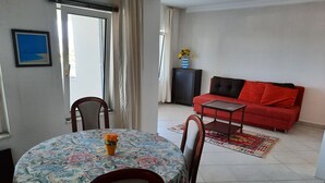 Un comedor con una mesa redonda y sillas, un sofá, un mueble para televisión y una ventana con cortinas.