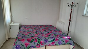 Un dormitorio pequeño y ordenado con una cama, una mesita de noche y un perchero.