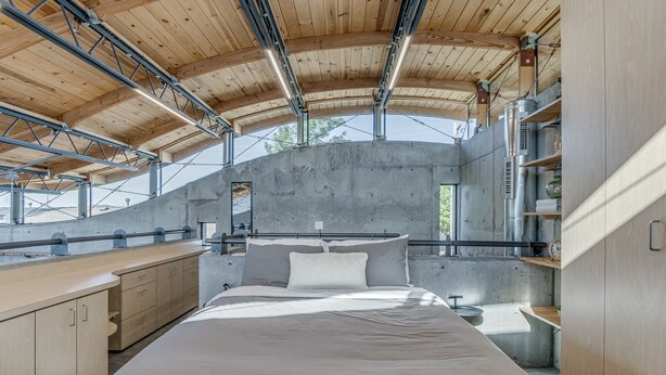 A modern bedroom with a large bed, wooden ceiling beams, and a concrete wall. - NEW INDUSTRIAL STUDIO - walking distance to UCO! (Edmond)