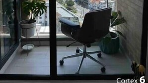 Un moderno spazio ufficio con un'ampia finestra vista sulla città, una sedia da ufficio nera e piante in vaso.