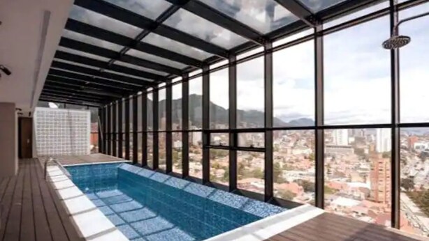 Una piscina interna moderna con vista sulla città, ampie finestre e un pontile in legno.