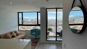 Un soggiorno moderno con divano, zona pranzo e ampie finestre con vista sulla città.