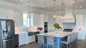 Una cocina amplia con una isla grande, armarios blancos, electrodomésticos de acero inoxidable y techo de madera.