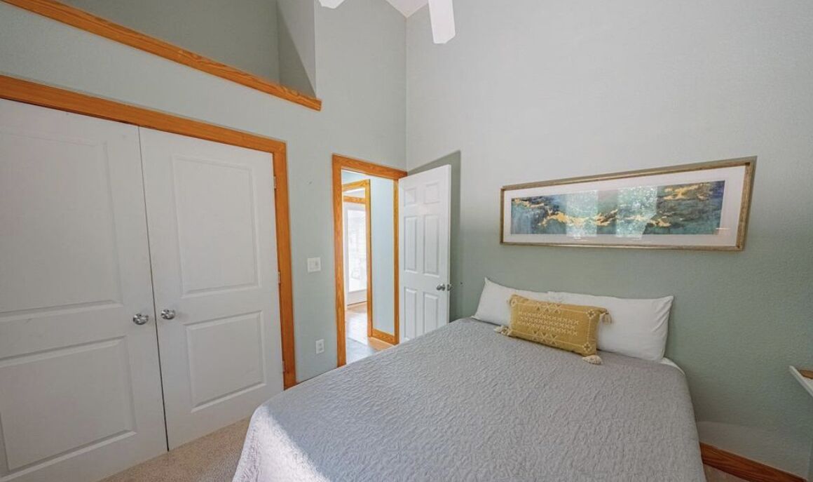 A bedroom with a bed, a framed artwork on the wall, and a door leading to another room.