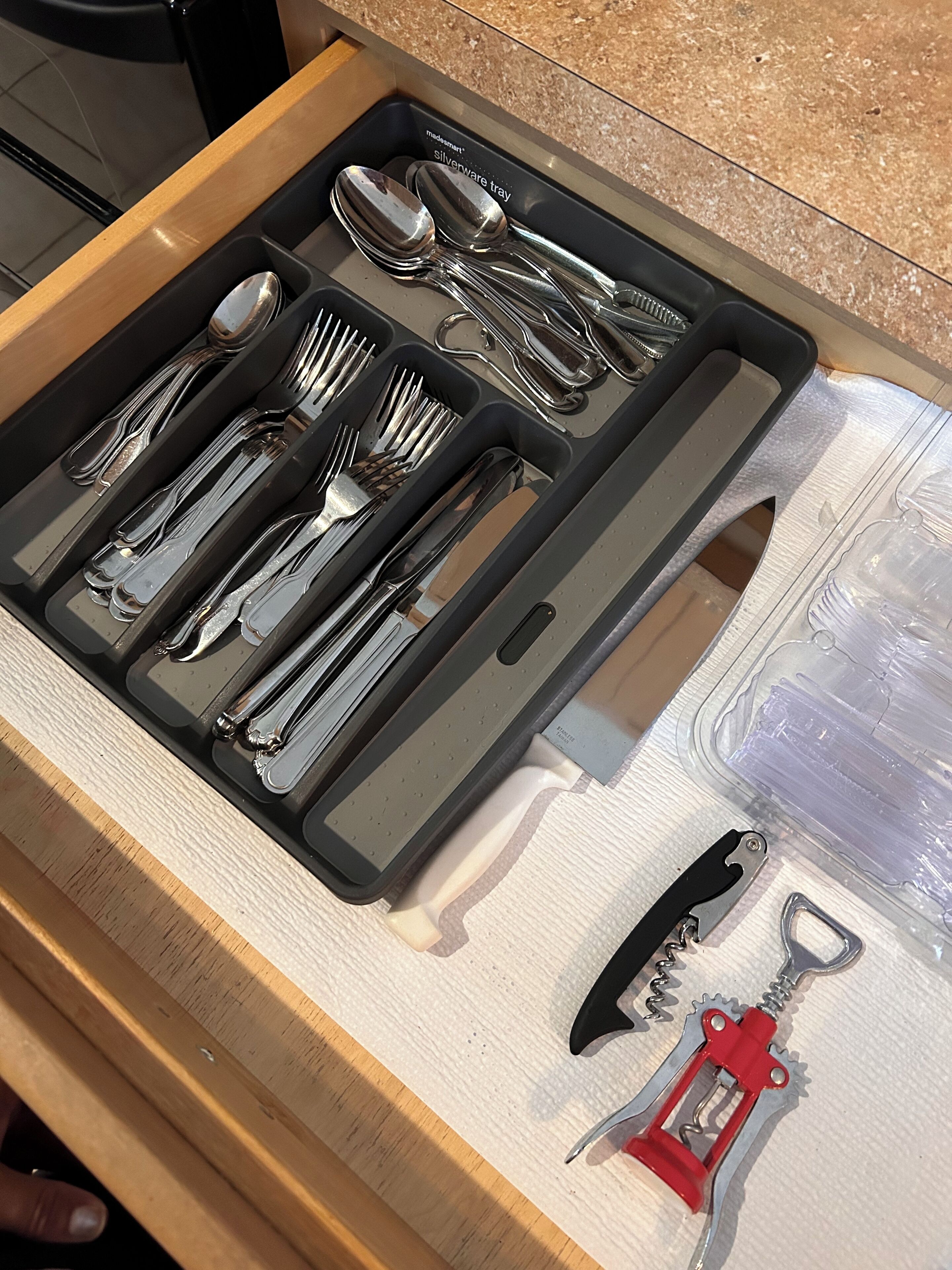 A drawer containing a set of silverware, including forks, knives, and spoons, along with a bottle opener and a corkscrew.