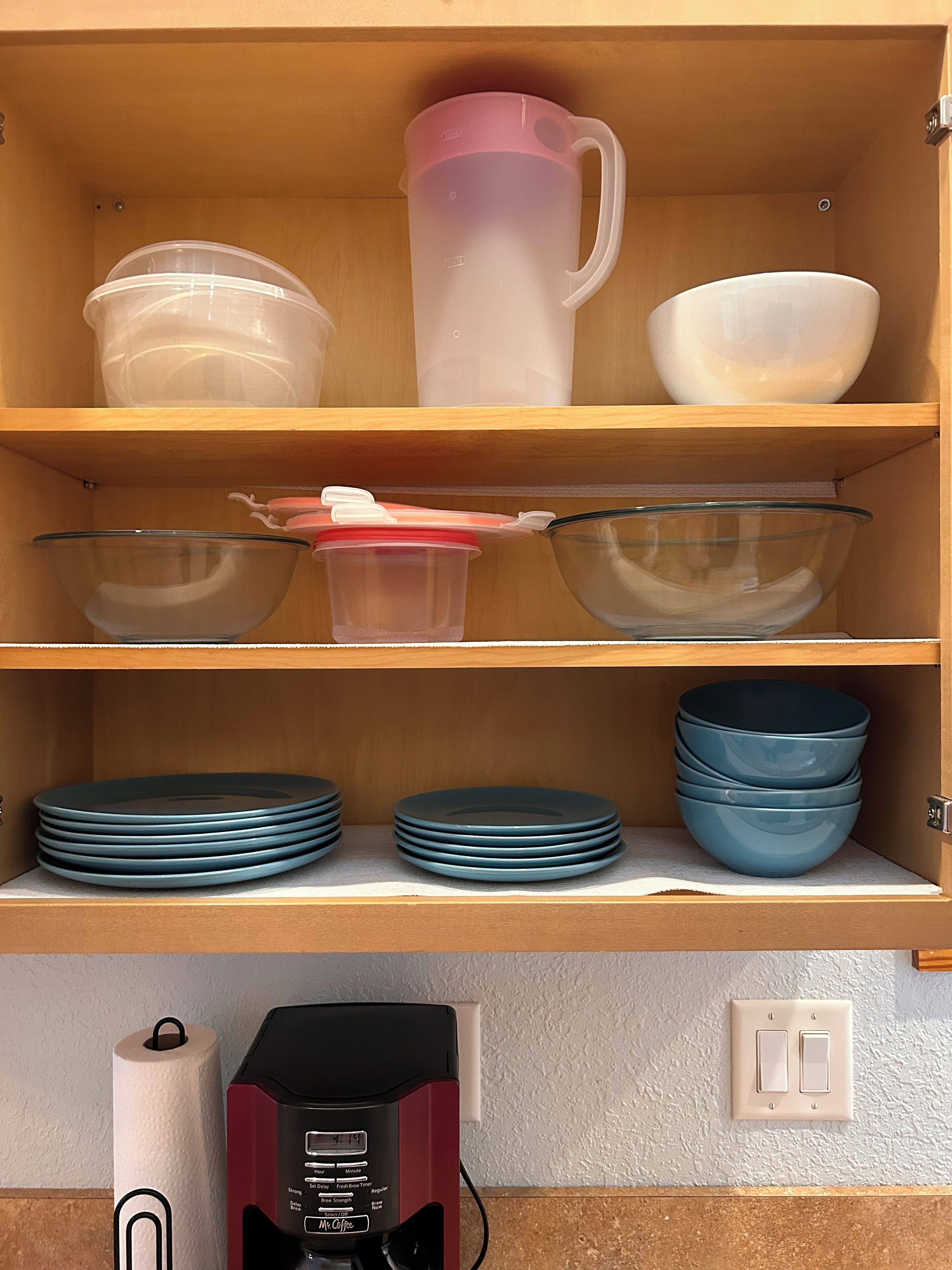 A kitchen shelf with storage containers, a coffee maker, and stacked plates.