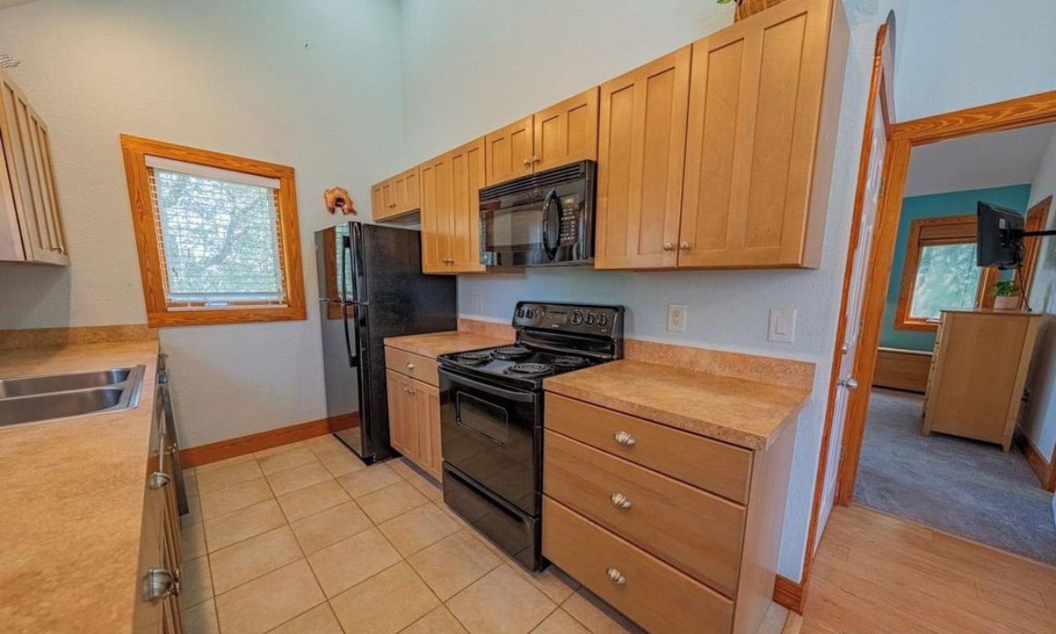 A kitchen with wooden cabinets, a black stove, a microwave, and a refrigerator.