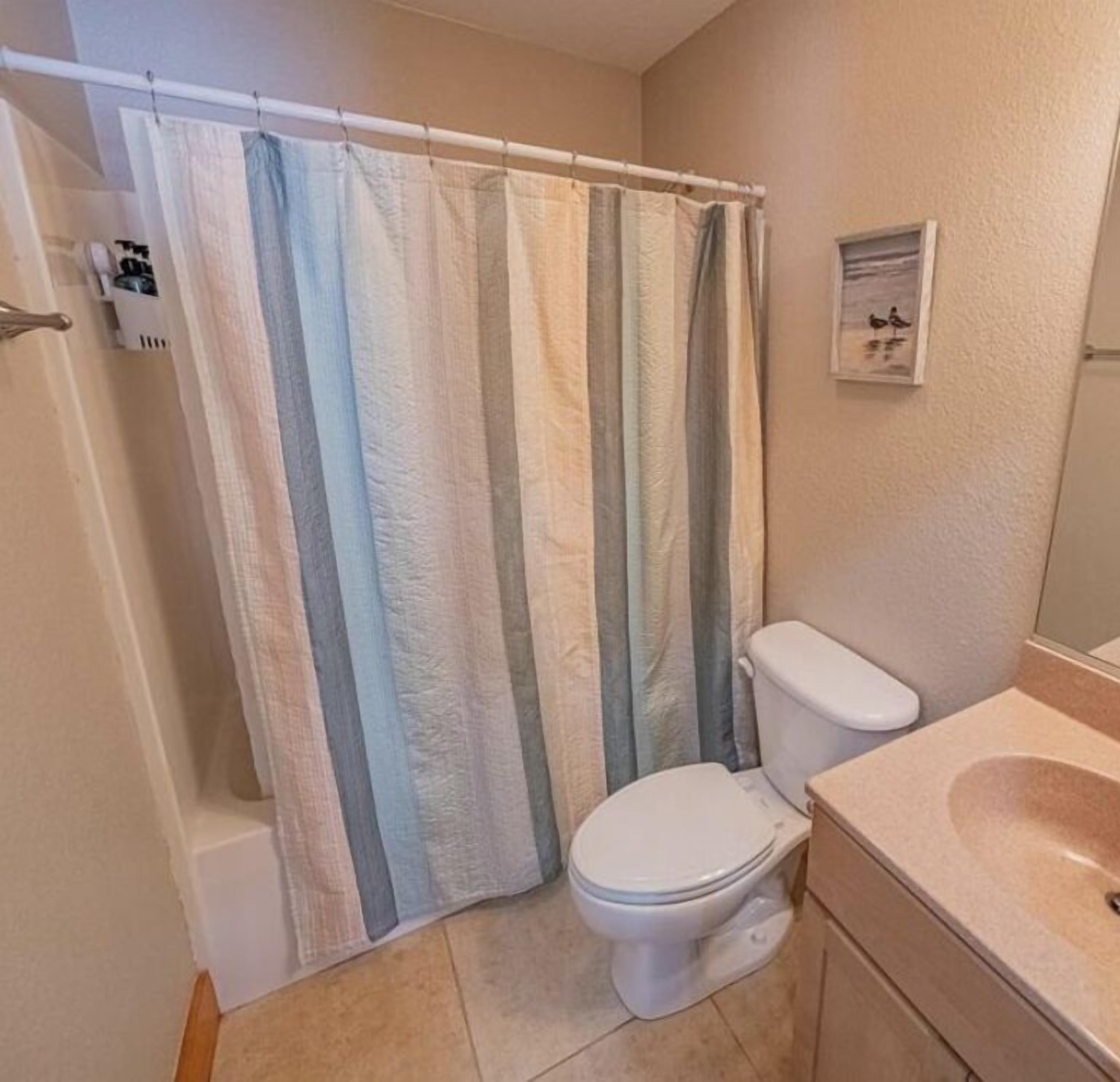 A bathroom with a shower curtain, toilet, and sink.
