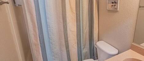A bathroom with a shower curtain, toilet, and sink.