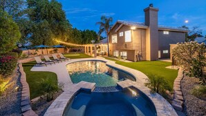 Una casa moderna con piscina, patio con sedie a sdraio e prato curato.
