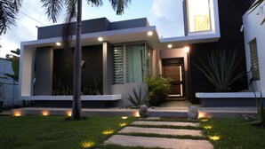 Een modern huis met een goed verlichte ingang, een groot raam en een pad dat naar de deur leidt.