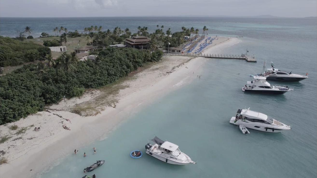 A beachside property with boats docked, a pier, and a beach with palm trees.