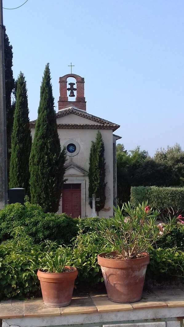 A small church with a bell tower, surrounded by greenery and potted plants.