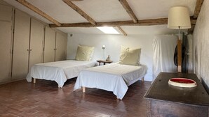 Una habitación con dos camas individuales, vigas de madera en el techo, una mesita con una lámpara y un espejo con marco rojo.