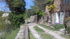 Un sendero estrecho de paredes de piedra que conduce a un rústico edificio de piedra con cerca de madera y follaje.