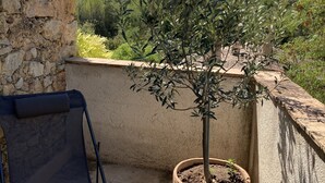 Un balcón con olivo en maceta, una silla plegable azul y una pared de piedra.