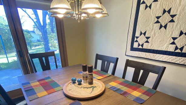 Una mesa de comedor con un mantel individual colorido, un juego de mesa de madera y un colcha colgada en la pared.