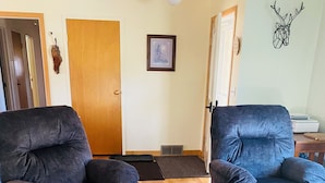 Una sala de estar con dos sillones azul oscuro, un sillón color beige, una mesa de centro de madera y un cuadro enmarcado en la pared.