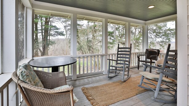 A covered porch with wicker furniture, a table, and a rocking chair. - Beautiful French Inspired Country Home Super Private River Views (Gambier)