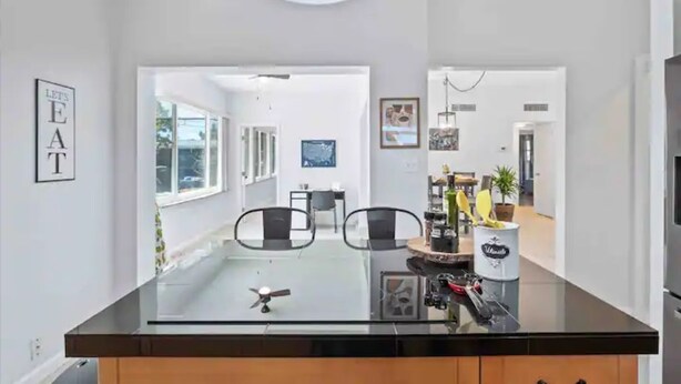 A modern kitchen with a glass-top island, black chairs, and a ceiling fan.