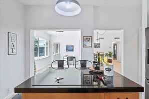 Une cuisine moderne dotée d’un îlot central avec un plan de travail en verre, de chaises noires et d’un ventilateur de plafond.