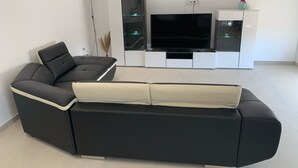Una sala de estar moderna con un sofá seccional negro, un televisor de pantalla plana y un mueble de entretenimiento blanco.