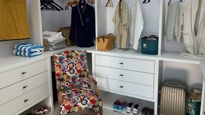 Un armario bien organizado con repisas, espacio para colgar y cajones, que contiene ropa doblada, zapatos y una silla estampada.