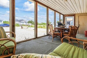 Eine überdachte Terrasse mit Korbmöbeln, einem Tisch und einem Grill.