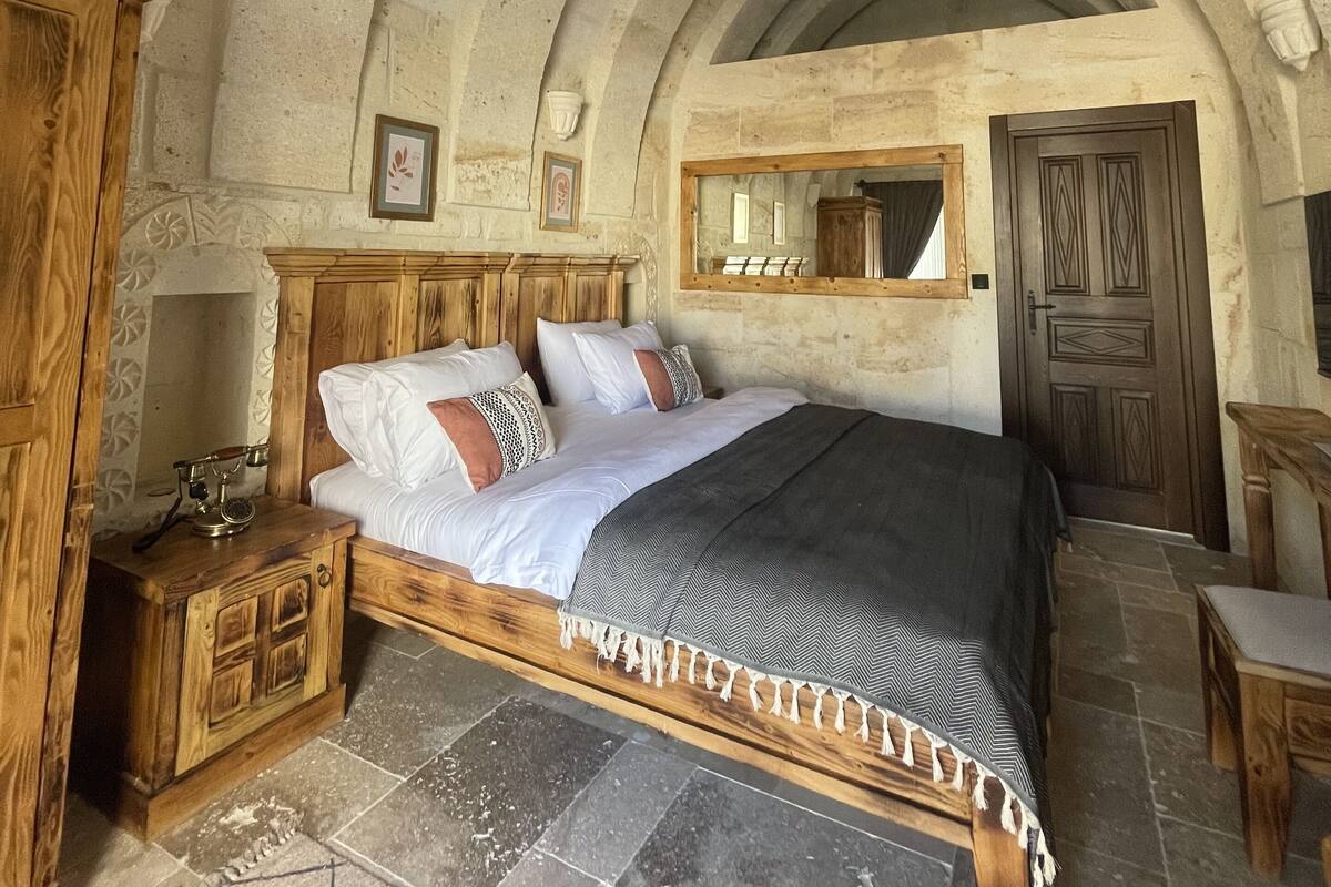 A bedroom with a stone vaulted ceiling, a wooden bed with a patterned bedspread, a nightstand, and a wooden wardrobe.