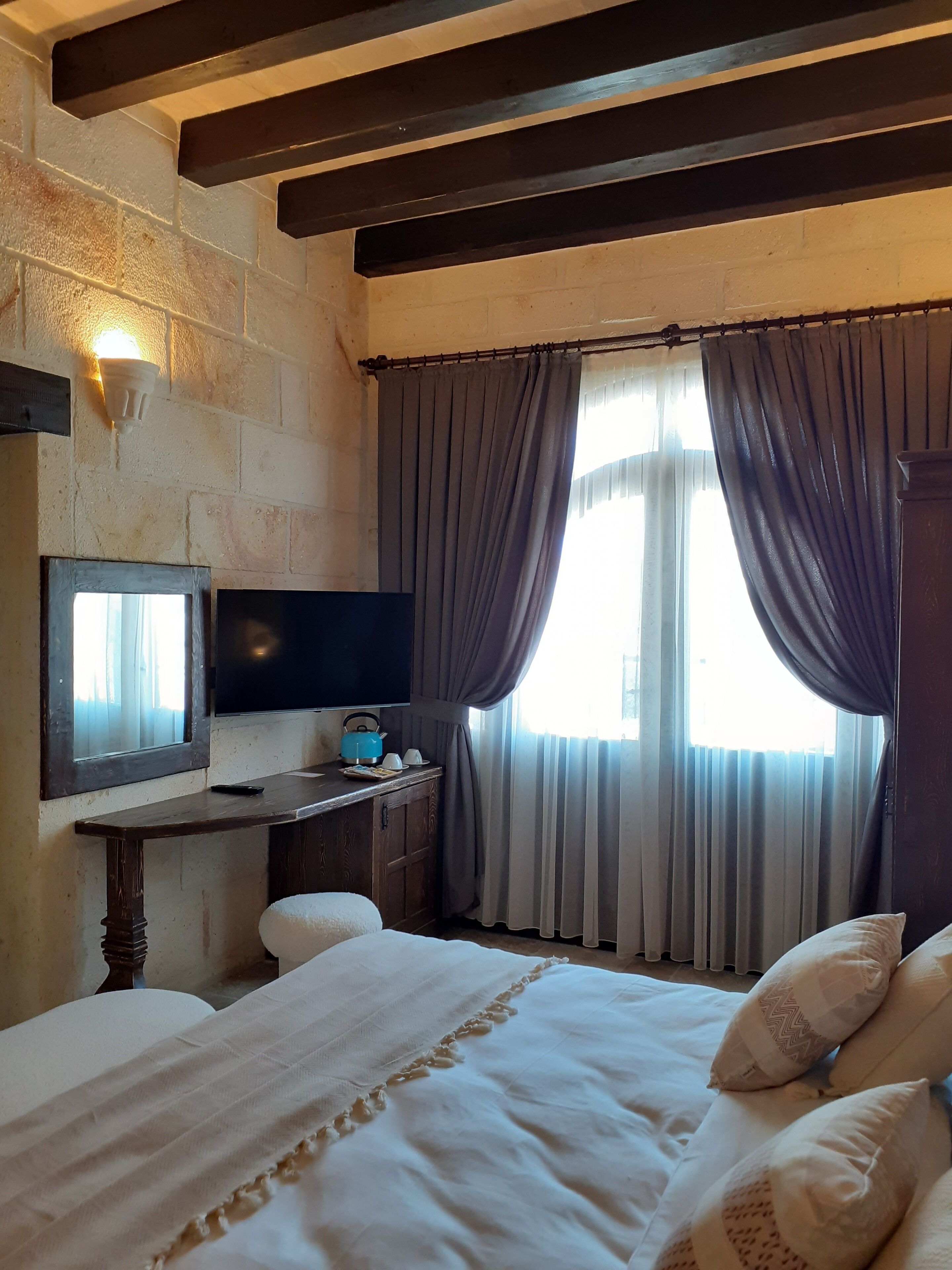 Un dormitorio con cama, televisor de pantalla plana, escritorio de madera y ventana con cortinas.