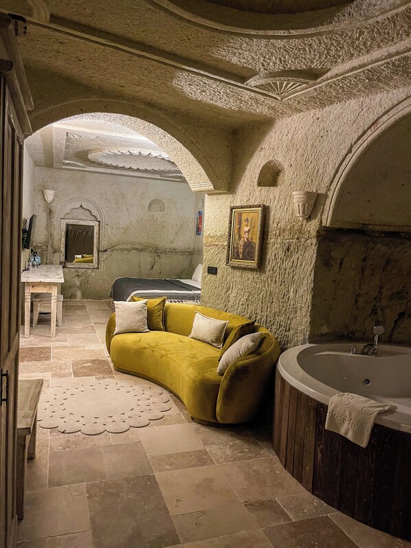 A room with a yellow sofa, a bathtub, and a small table with a chair.
