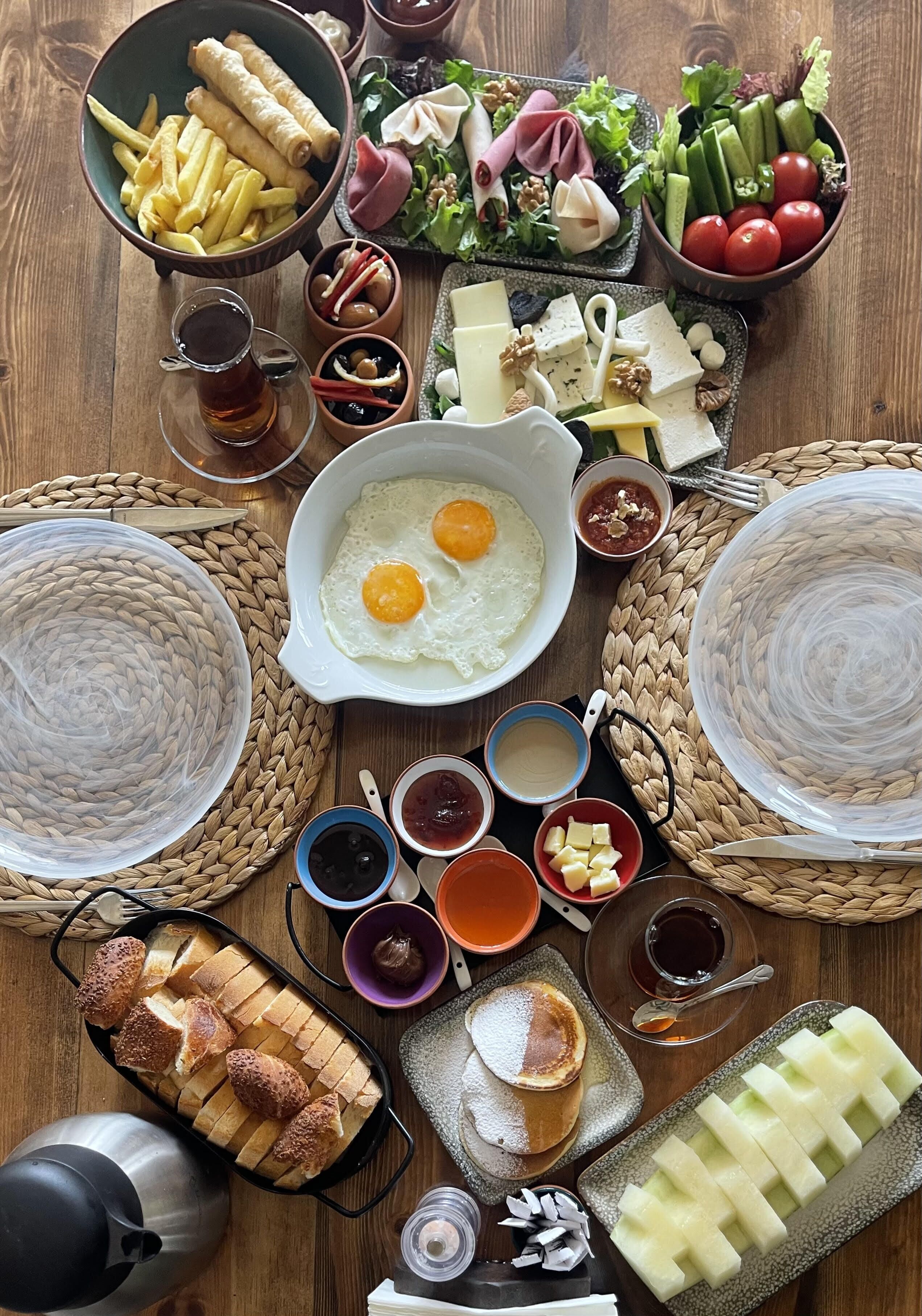 Ein Tisch mit verschiedenen Speisen, darunter Eier, Käse und Brot, auf einer Holztischplatte.