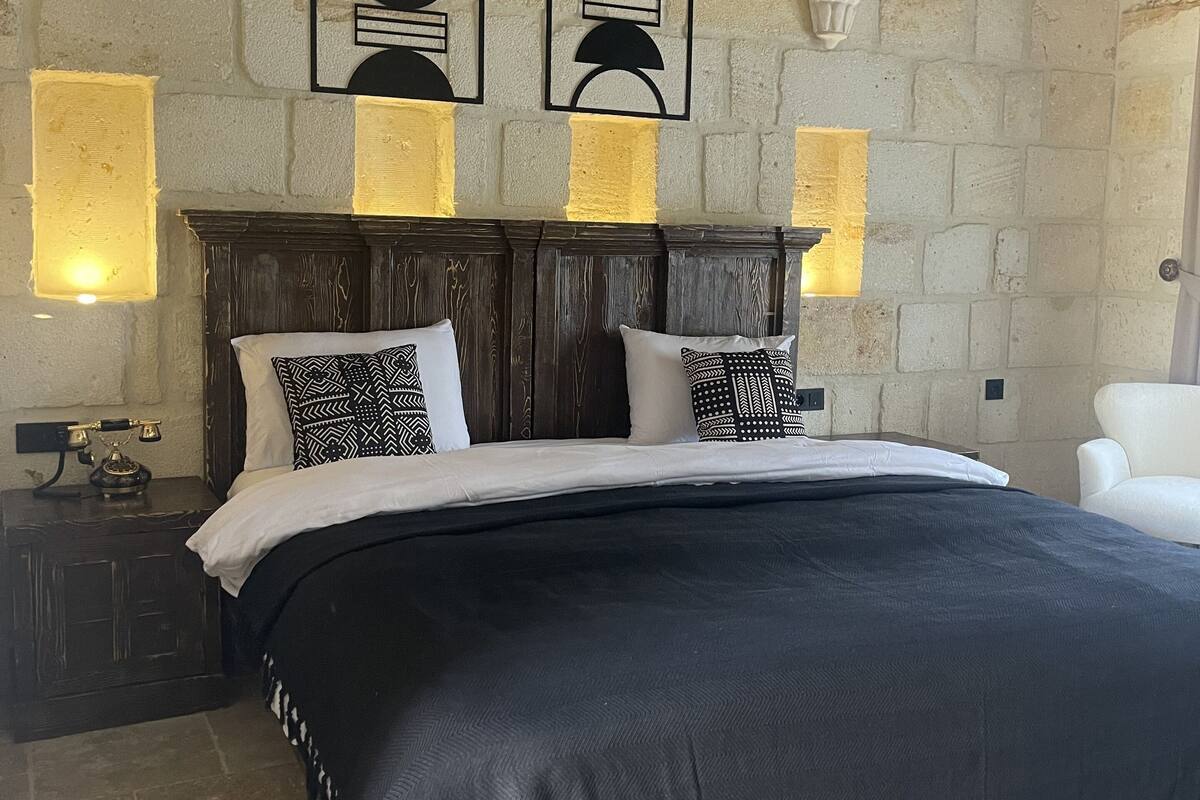 A bedroom with a stone wall, a wooden headboard, and a bed with black bedding.